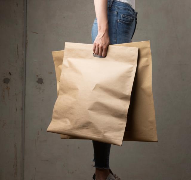 Embacollage - Bestseller - Woman holding brown bags in right hand, wearing blue jeans.