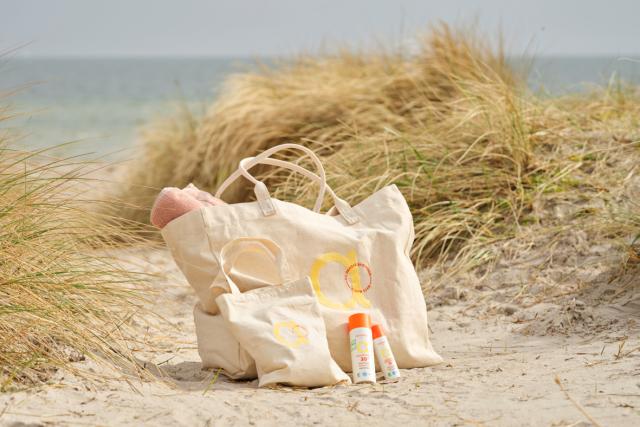 En obetat canvasväska med färgglad blomkrans och texten 'Shop ANIKI BEACH' tryckt i mitten mot en mörk bakgrund